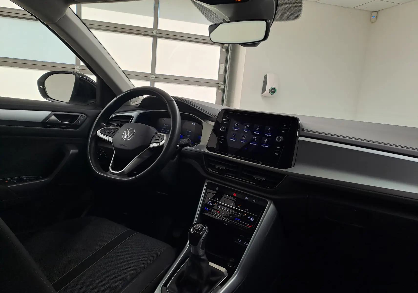 Vue intérieure côté conducteur du Volkswagen T-Roc 2022, tableau de bord noir avec écran tactile et levier de vitesses manuel.
