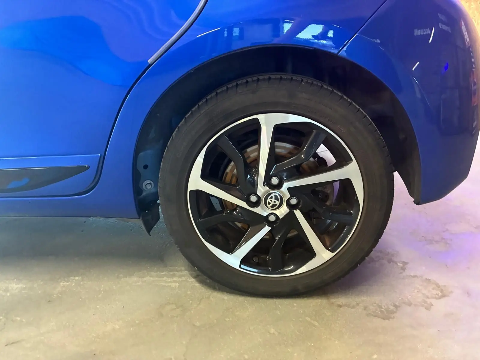 Gros plan sur la roue arrière droite d'une Toyota Yaris hybride bleue, mettant en valeur la jante alliage bicolore.