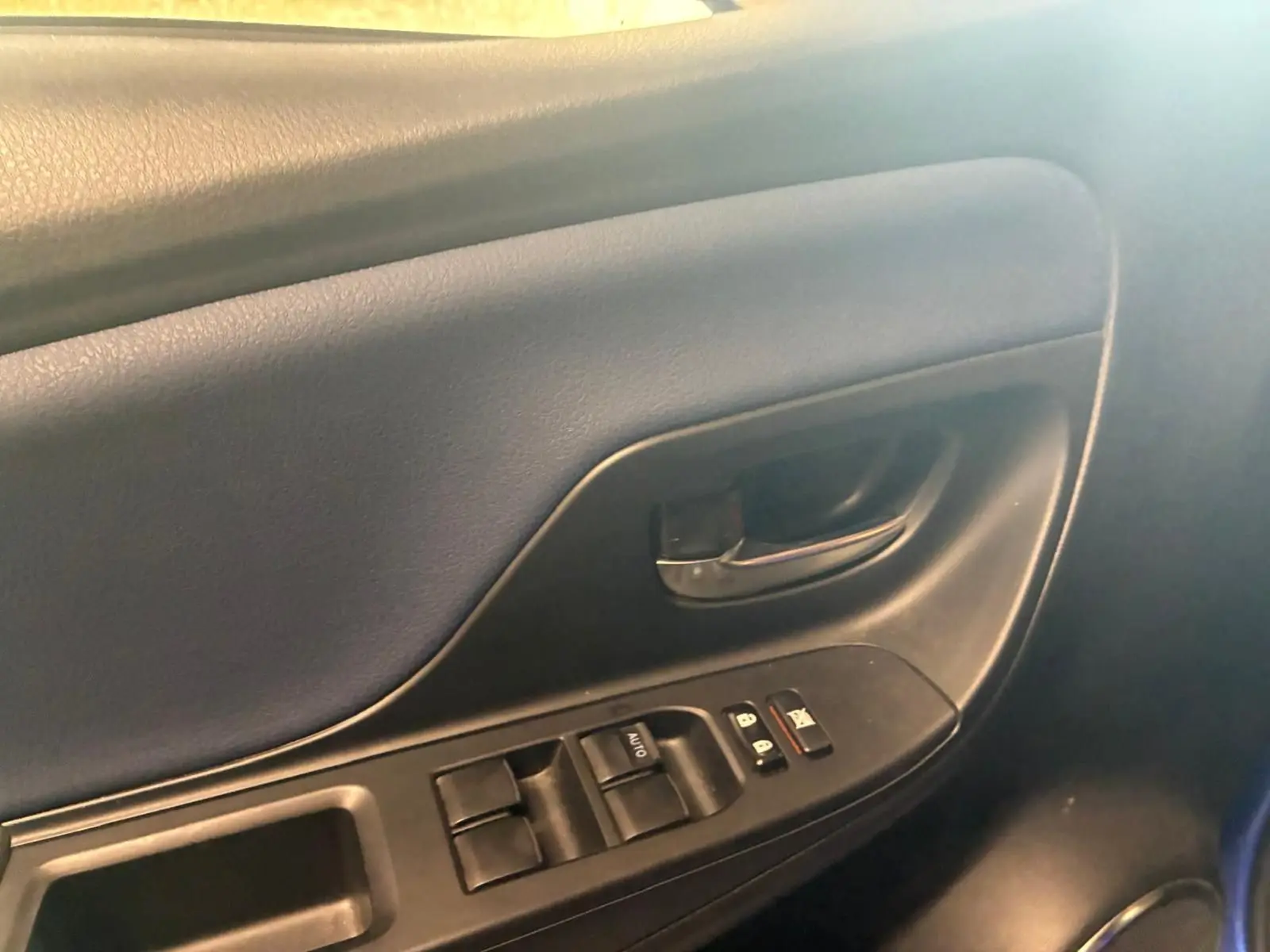 Gros plan sur la porte intérieure côté conducteur de la Toyota Yaris bleu, montrant les commandes des vitres et la poignée noire.
