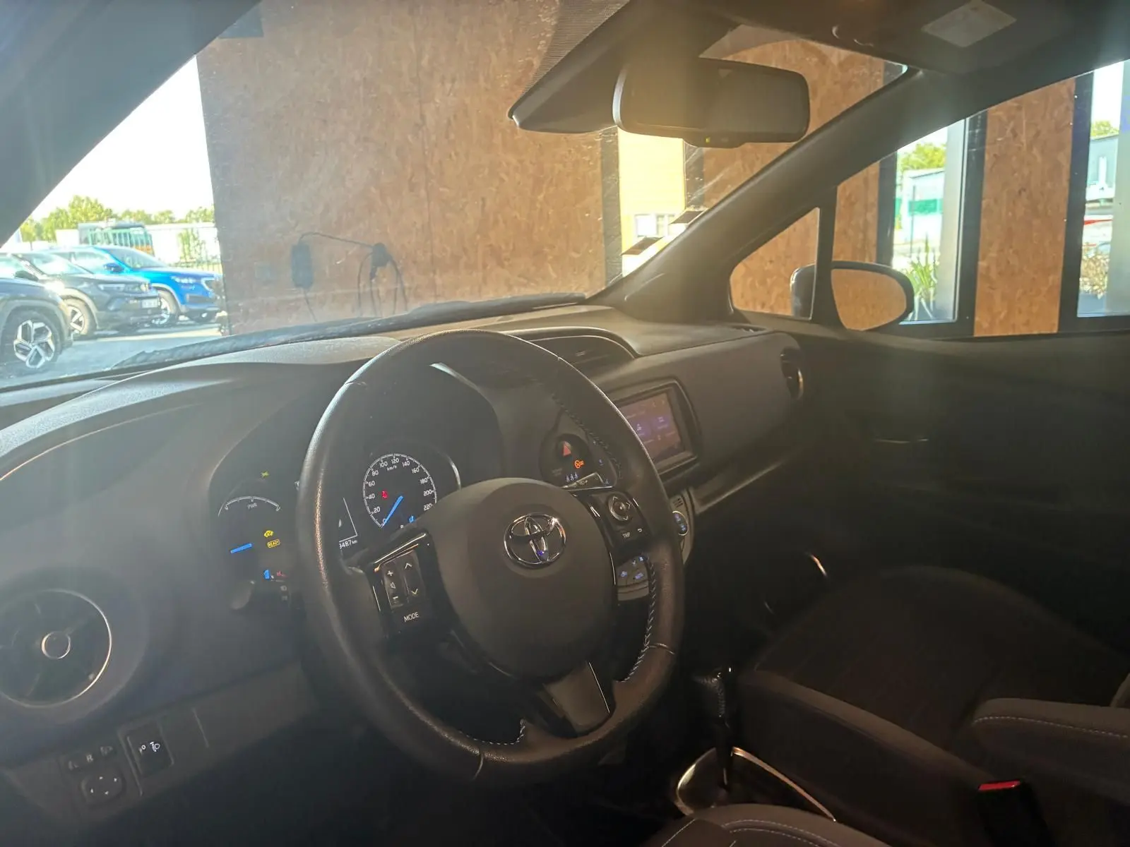 Vue intérieure côté conducteur de la Toyota Yaris hybride 2020, volant cuir noir et tableau de bord avec écran tactile.