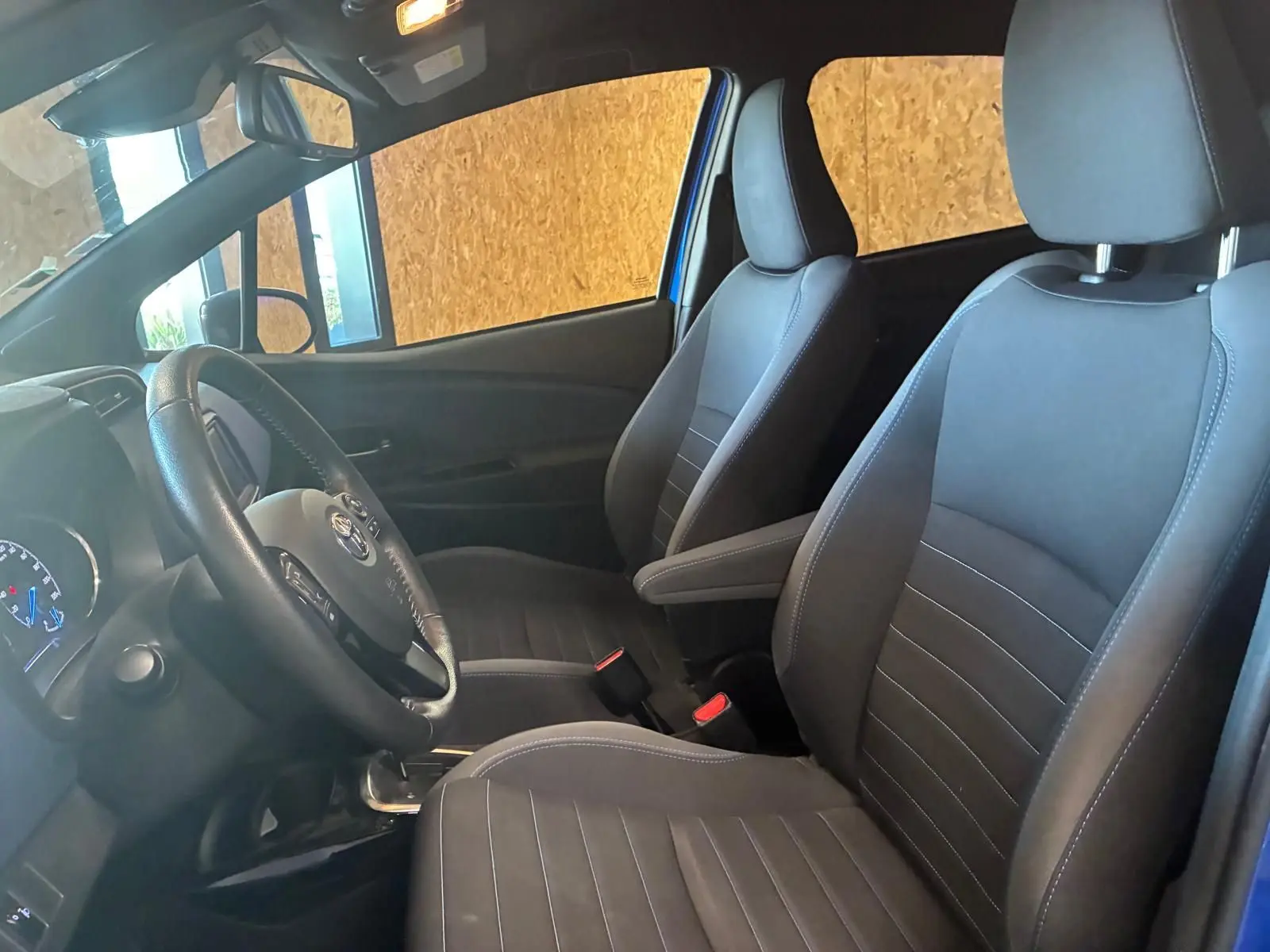 Vue intérieure côté conducteur de la Toyota Yaris hybride 2020, sièges tissu noir et volant multifonction.