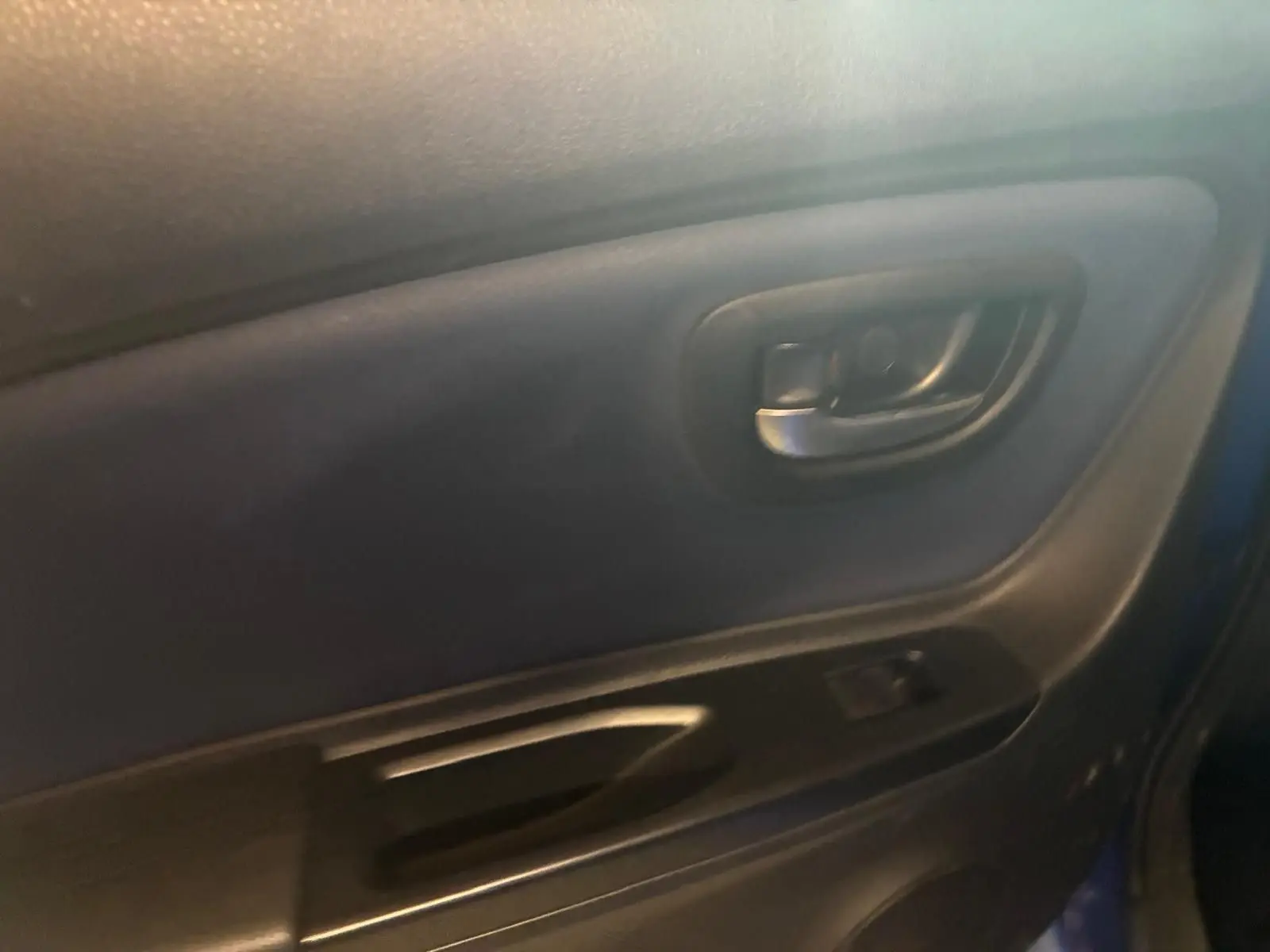 Gros plan sur la poignée intérieure et la commande de fenêtre de la porte côté gauche d’une Toyota Yaris bleu 2020.