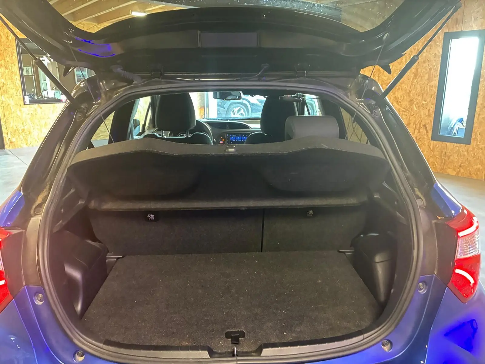 Vue arrière ouverte du coffre d’une Toyota Yaris hybride bleue 2020, intérieur noir et tablette de coffre visible.