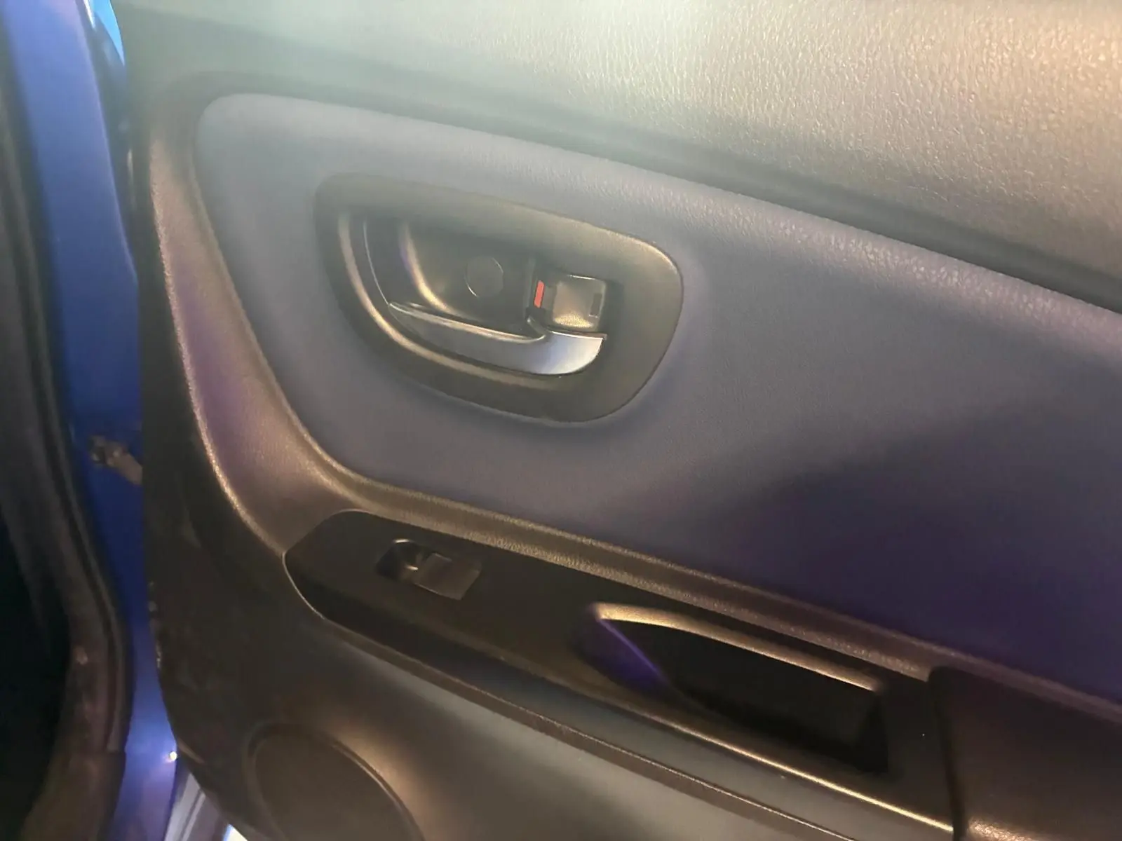 Gros plan sur la poignée intérieure et panneau de porte côté gauche d'une Toyota Yaris bleu 2020, finition hybride.