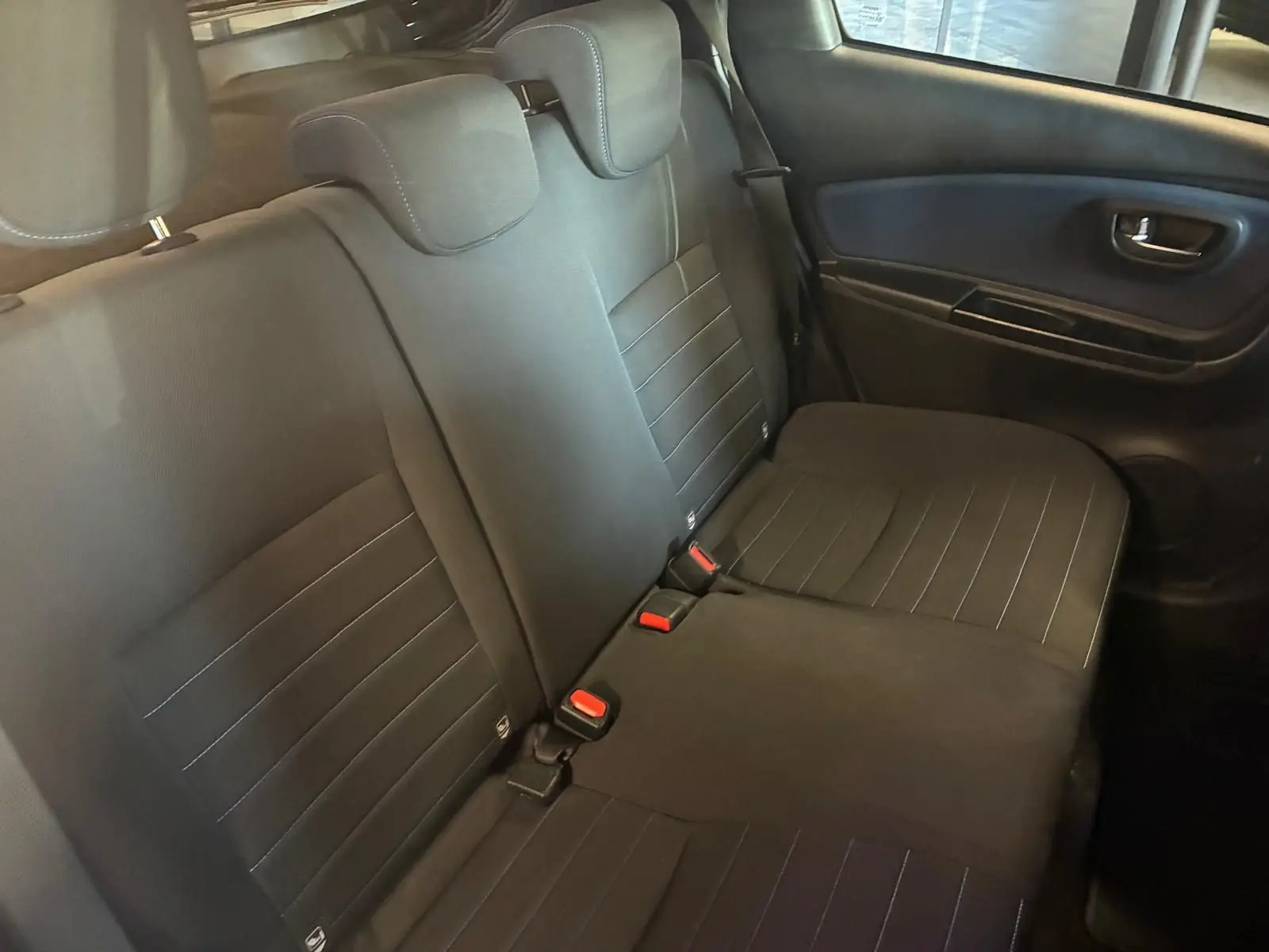 Vue intérieure du siège arrière côté droit de la Toyota Yaris hybride 2020 avec sellerie tissu noire et ceintures rouges.