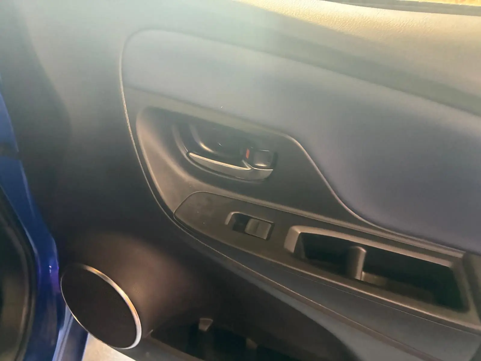 Vue intérieure du panneau de porte côté gauche d'une Toyota Yaris hybride bleue avec commande de vitre et poignée noire.