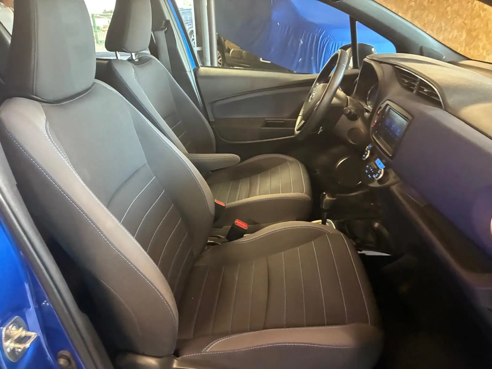 Intérieur de la Toyota Yaris 2020 bleu, vue côté gauche, sièges tissu noirs et tableau de bord avec écran tactile.