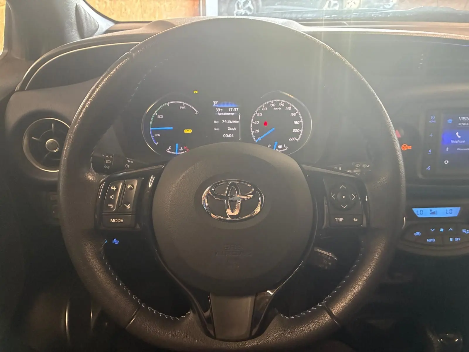 Vue rapprochée du volant noir de la Toyota Yaris hybride 2020 avec tableau de bord et écran tactile visibles.