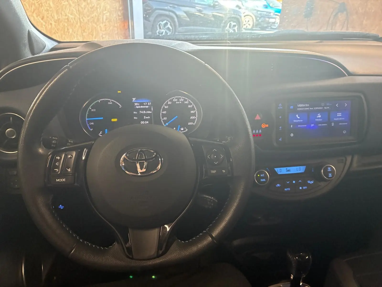 Vue intérieure centrée sur le volant de la Toyota Yaris hybride 2020 avec tableau de bord et écran tactile allumé.