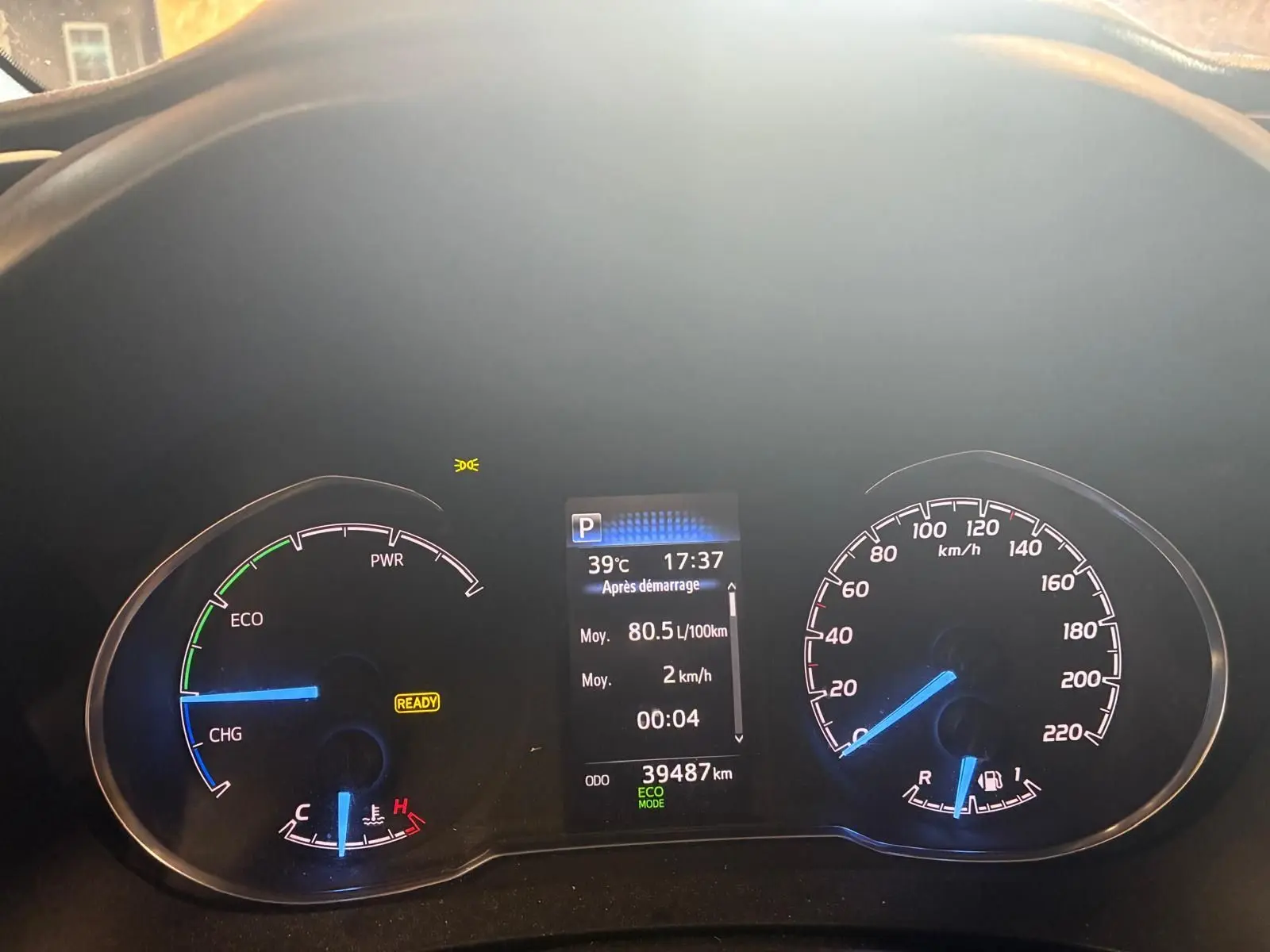 Vue rapprochée du tableau de bord numérique d'une Toyota Yaris hybride bleue, affichant la vitesse, la température et l'autonomie.