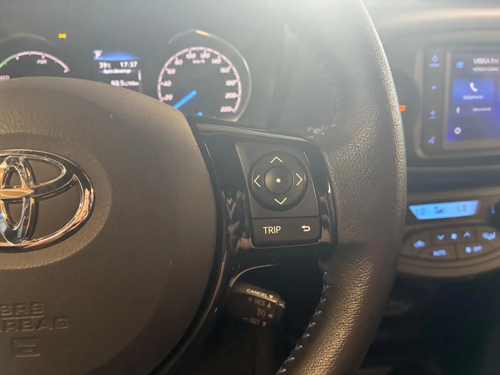 Gros plan sur le volant noir de la Toyota Yaris 2020 avec commandes multifonctions et tableau de bord lumineux en arrière-plan.