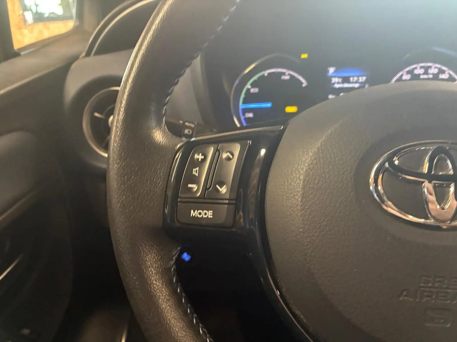 Gros plan sur le volant noir de la Toyota Yaris 2020 avec commandes intégrées et tableau de bord hybride en arrière-plan.