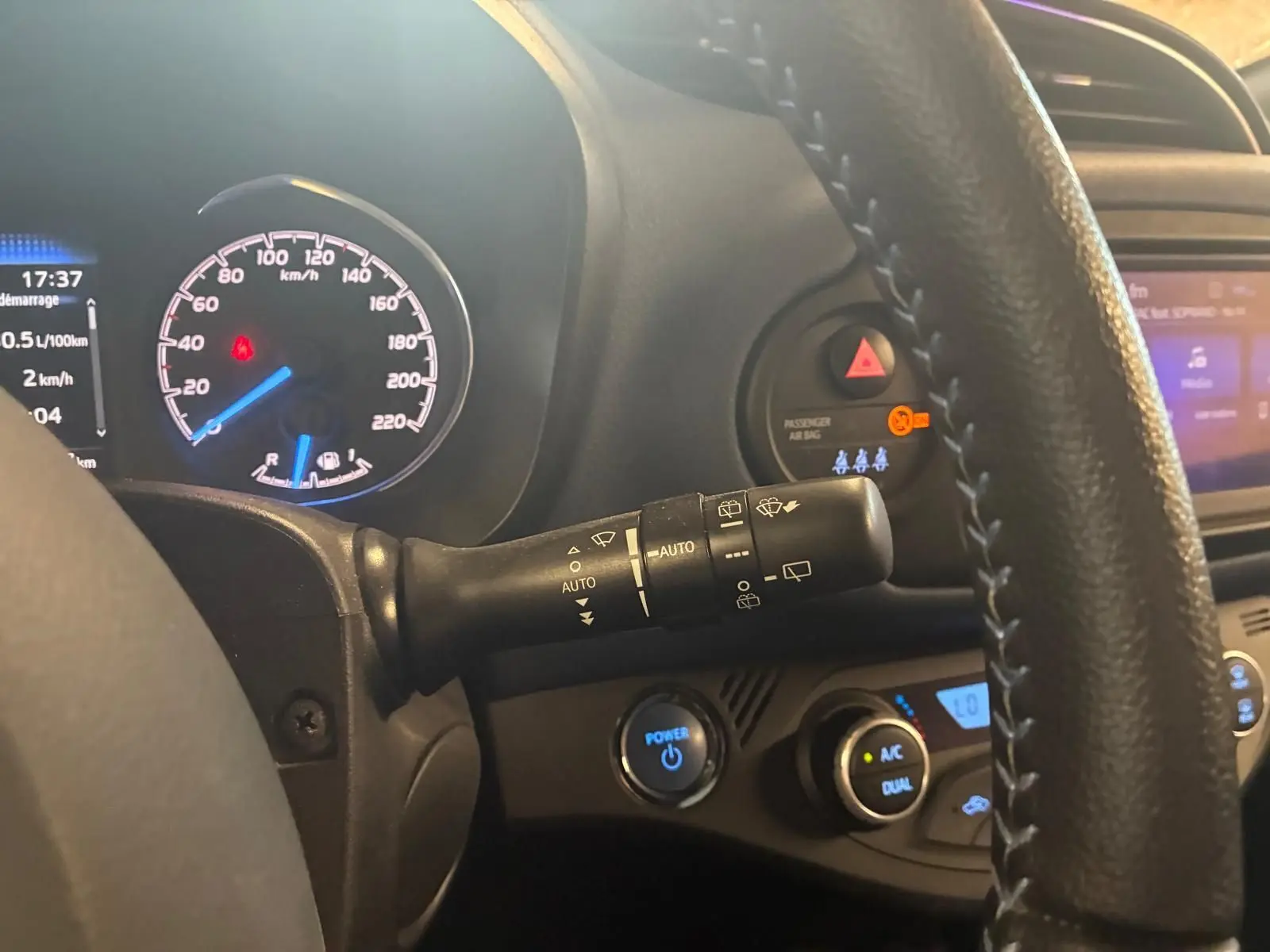 Vue intérieure centrée sur le combiné d'instruments et le commodo d'essuie-glace d'une Toyota Yaris hybride bleue de 2020.