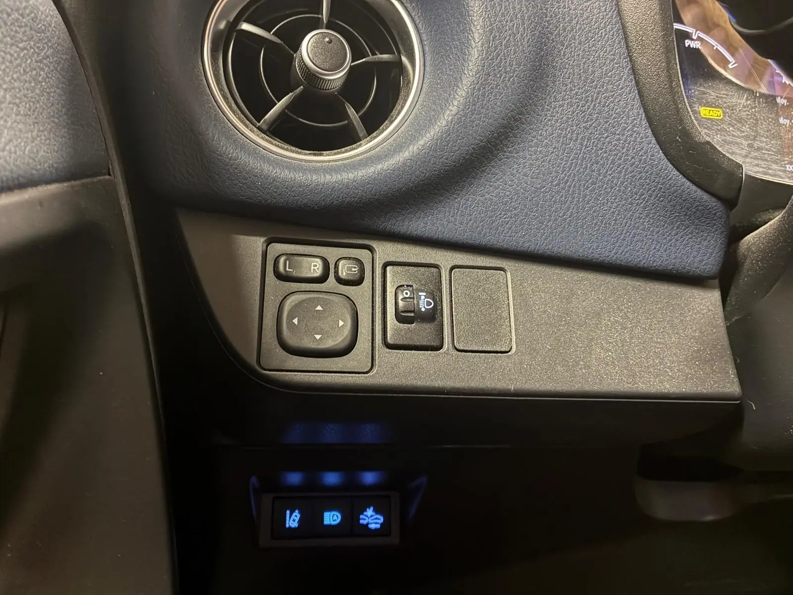 Détail intérieur côté gauche du tableau de bord bleu de la Toyota Yaris 2020, avec commandes des rétroviseurs et réglage des phares.
