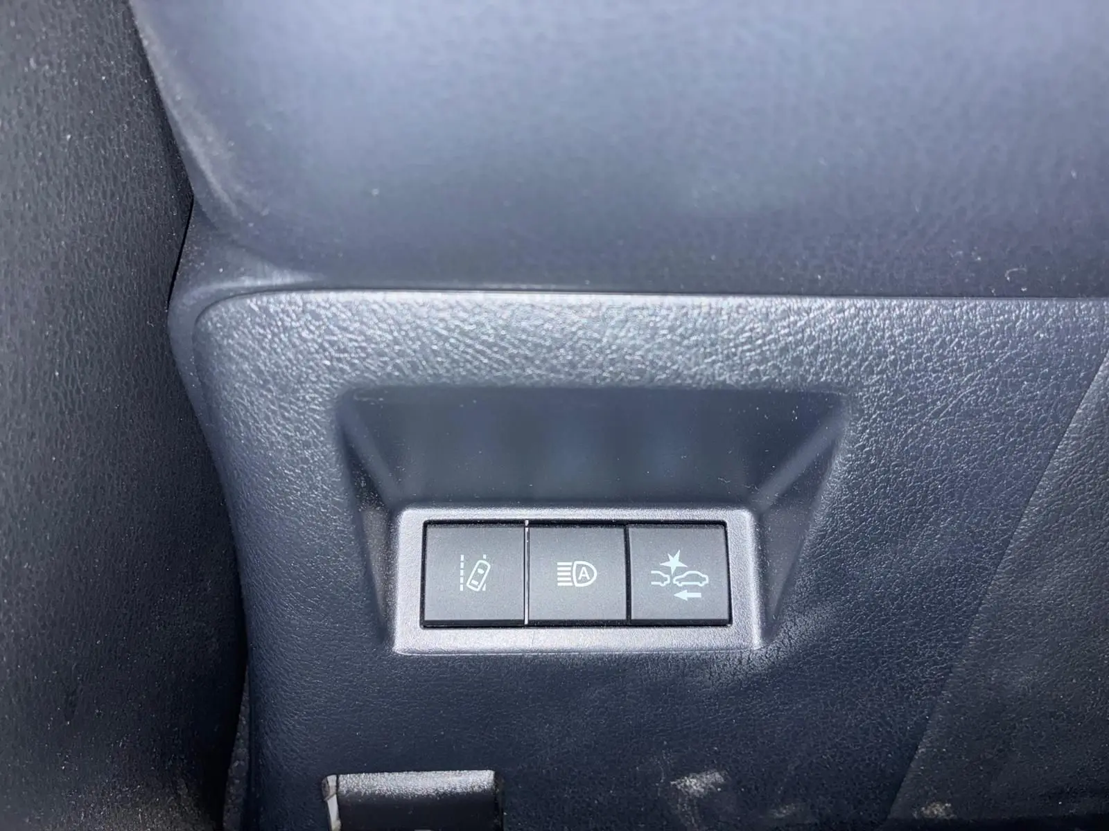 Gros plan sur les trois boutons de commande situés à gauche du tableau de bord dans une Toyota Yaris hybride bleue de 2020.