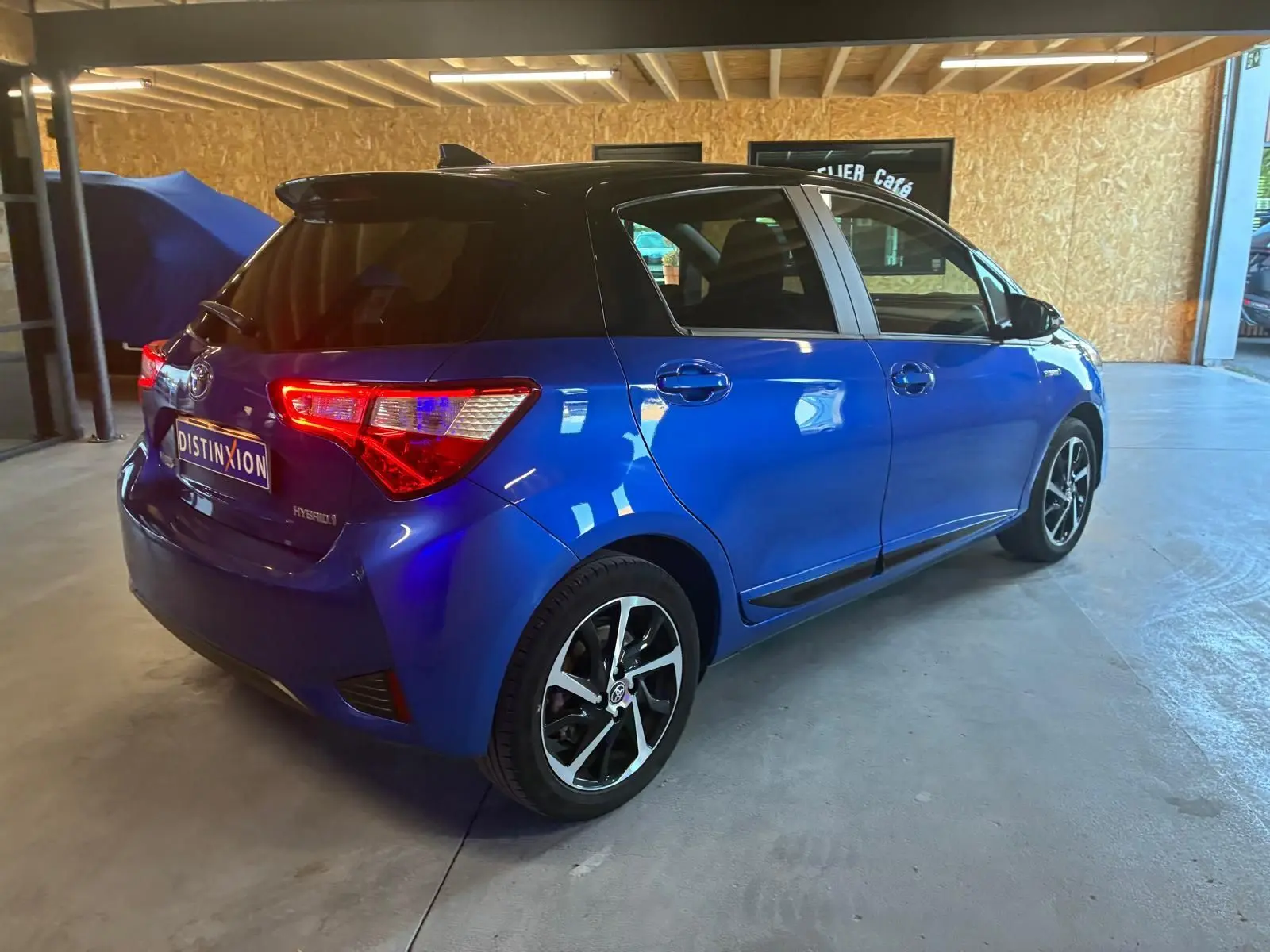 Vue 3/4 arrière droite d'une Toyota Yaris hybride bleue 5 portes avec jantes alliage et vitres teintées, stationnée en intérieur.