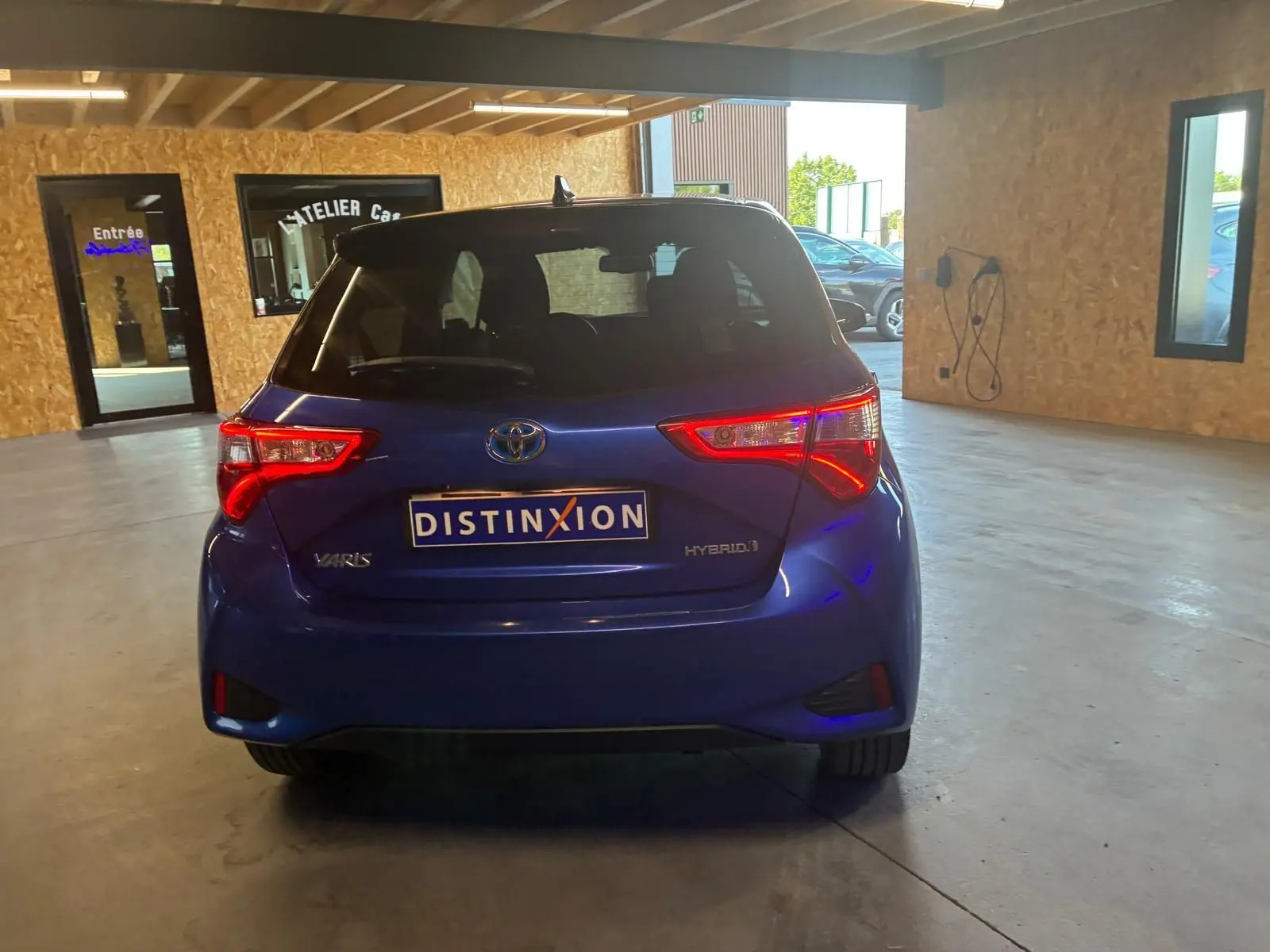 Vue arrière d'une Toyota Yaris hybride bleue 2020, avec feux arrière allumés dans un garage lumineux.