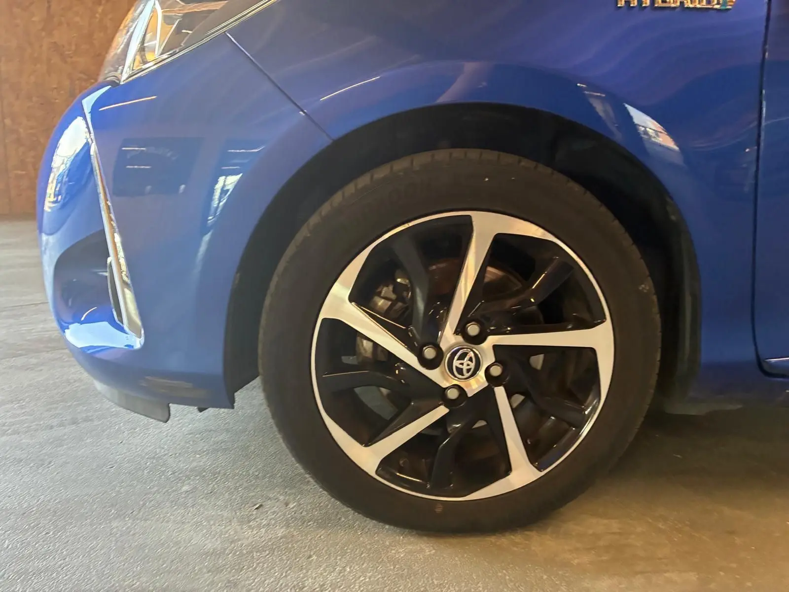 Gros plan sur la roue avant gauche d'une Toyota Yaris hybride bleue 2020, avec jante alliage bicolore et logo Toyota visible.