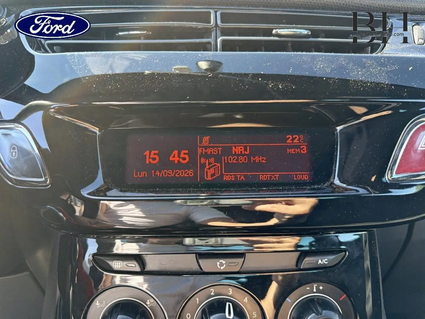 Gros plan sur la console centrale noire brillante de la Citroën DS3 rouge Rubi, affichant l’horloge et la radio FM.