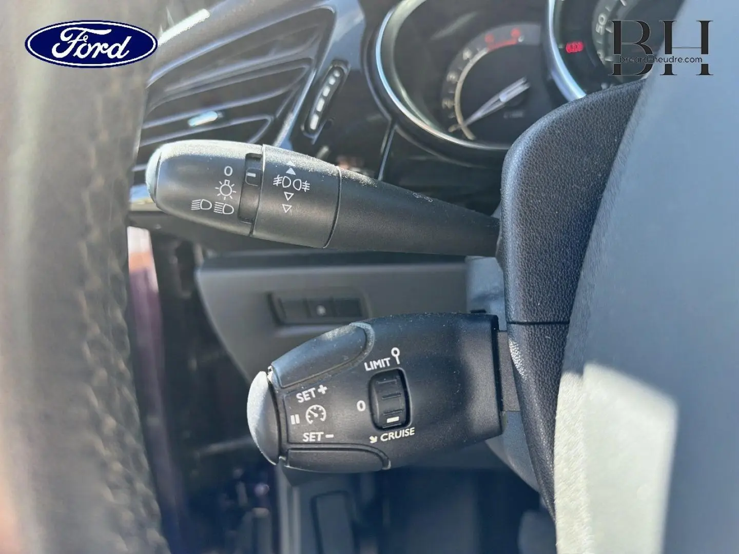 Gros plan sur la commande de régulateur de vitesse et des feux, intérieur noir du volant d'une Citroën DS3 rouge Rubi.