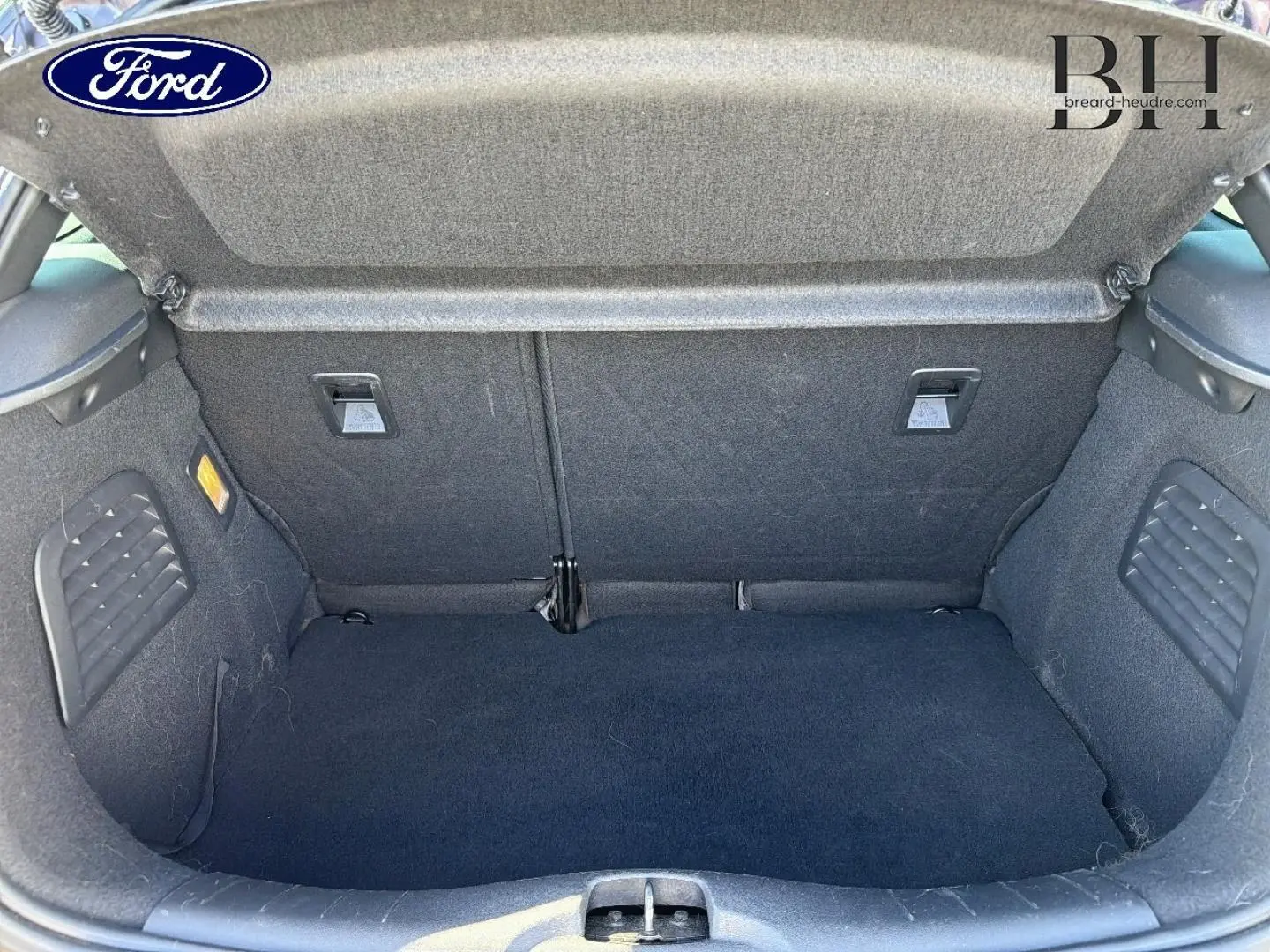Coffre ouvert vu de face d'une Citroën DS3 rouge Rubi, montrant l'espace de chargement et la moquette noire.