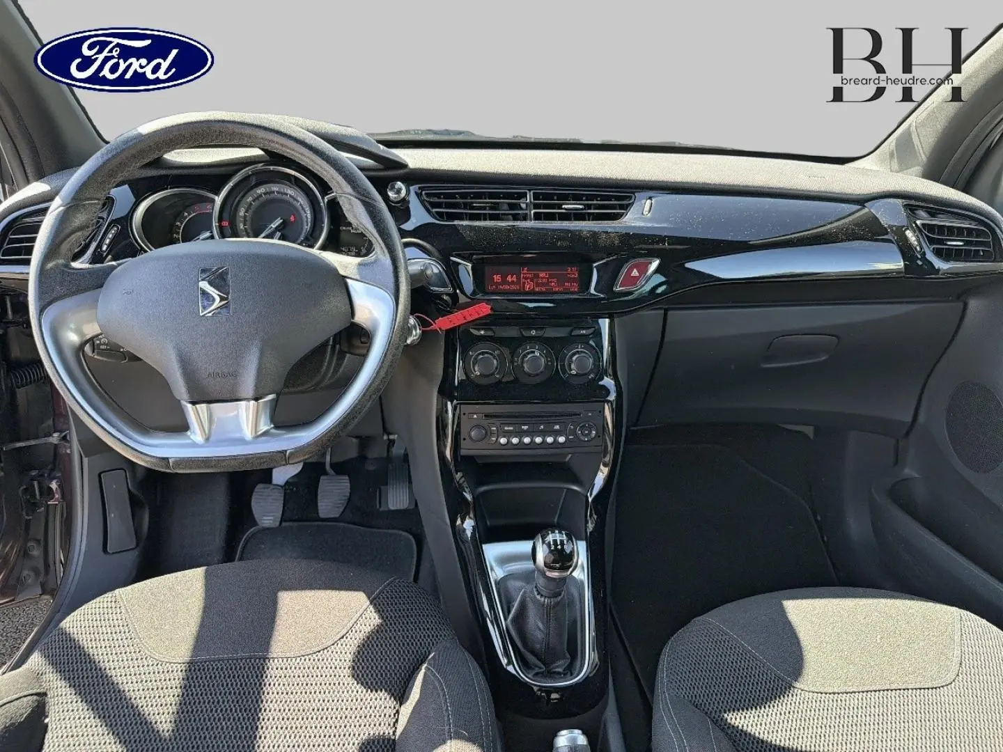 Vue intérieure avant du tableau de bord et volant DS3 avec levier de vitesse manuel, finition noire brillante et sièges gris.