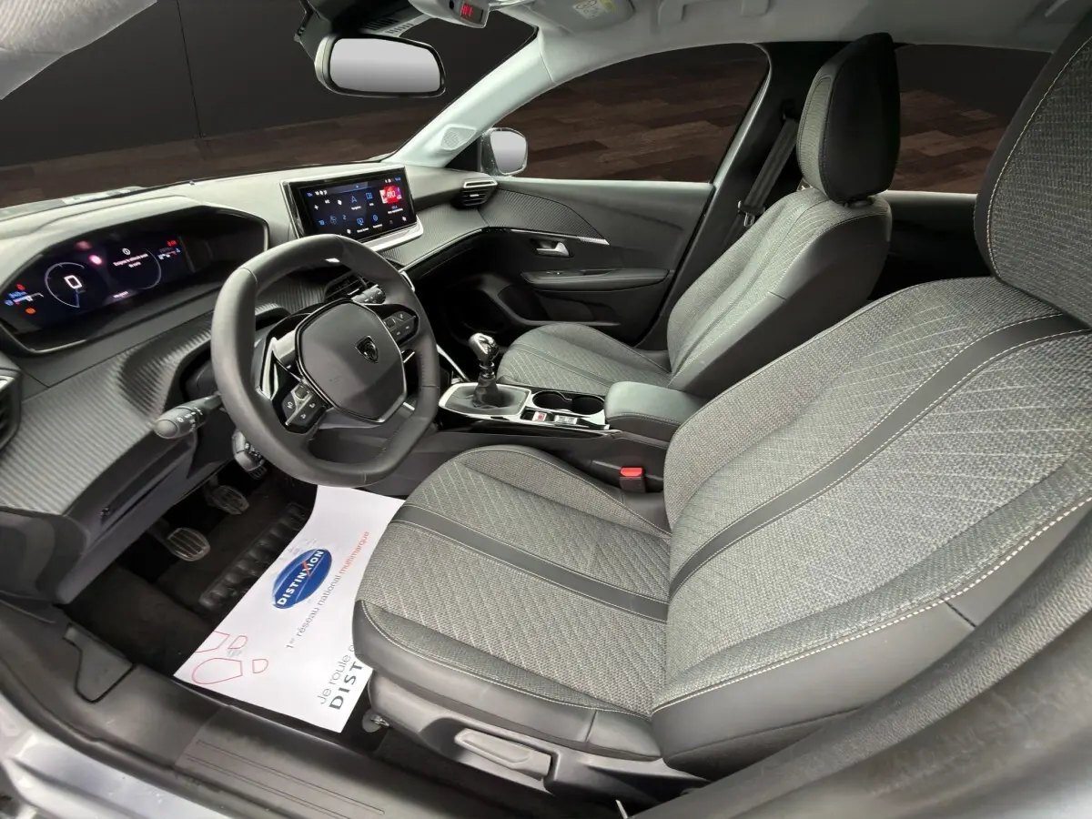 Vue intérieure côté conducteur de la Peugeot 208 gris clair, volant cuir multifonctions et sièges tissu gris avec surpiqûres.