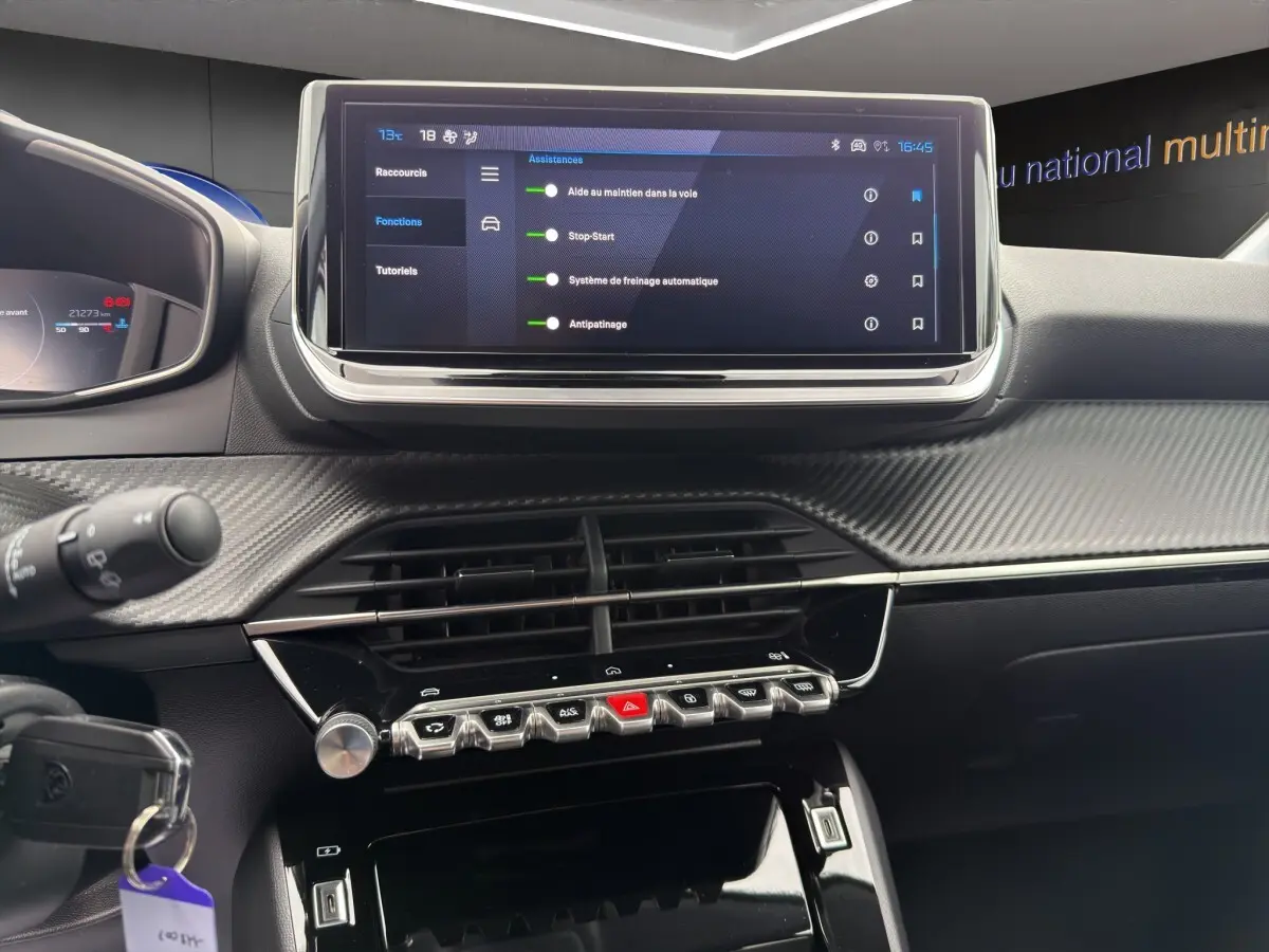Vue rapprochée du tableau de bord noir et carbone de la Peugeot 208 2025 avec écran tactile central et commandes piano.