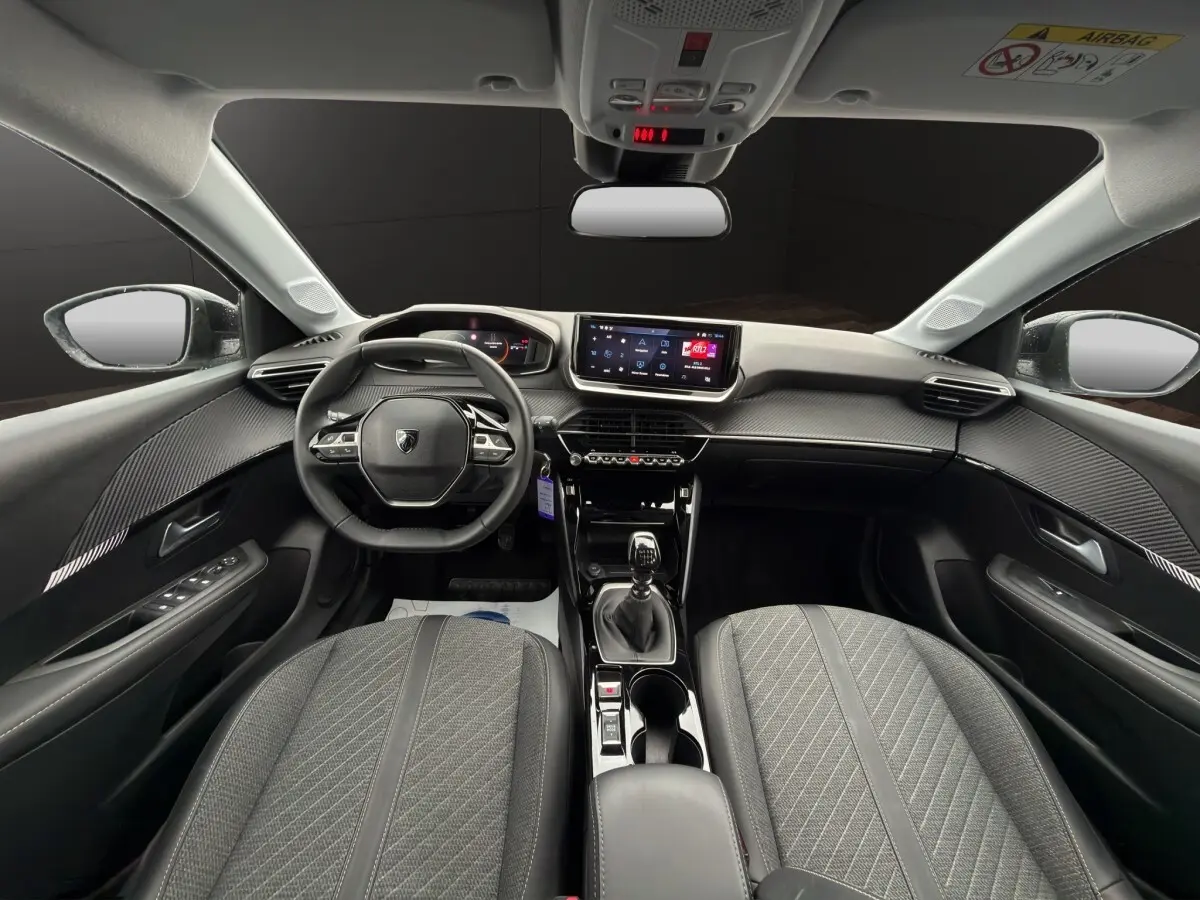 Vue intérieure avant de la Peugeot 208 2025 gris clair, volant cuir multifonctions et écran tactile central visible.