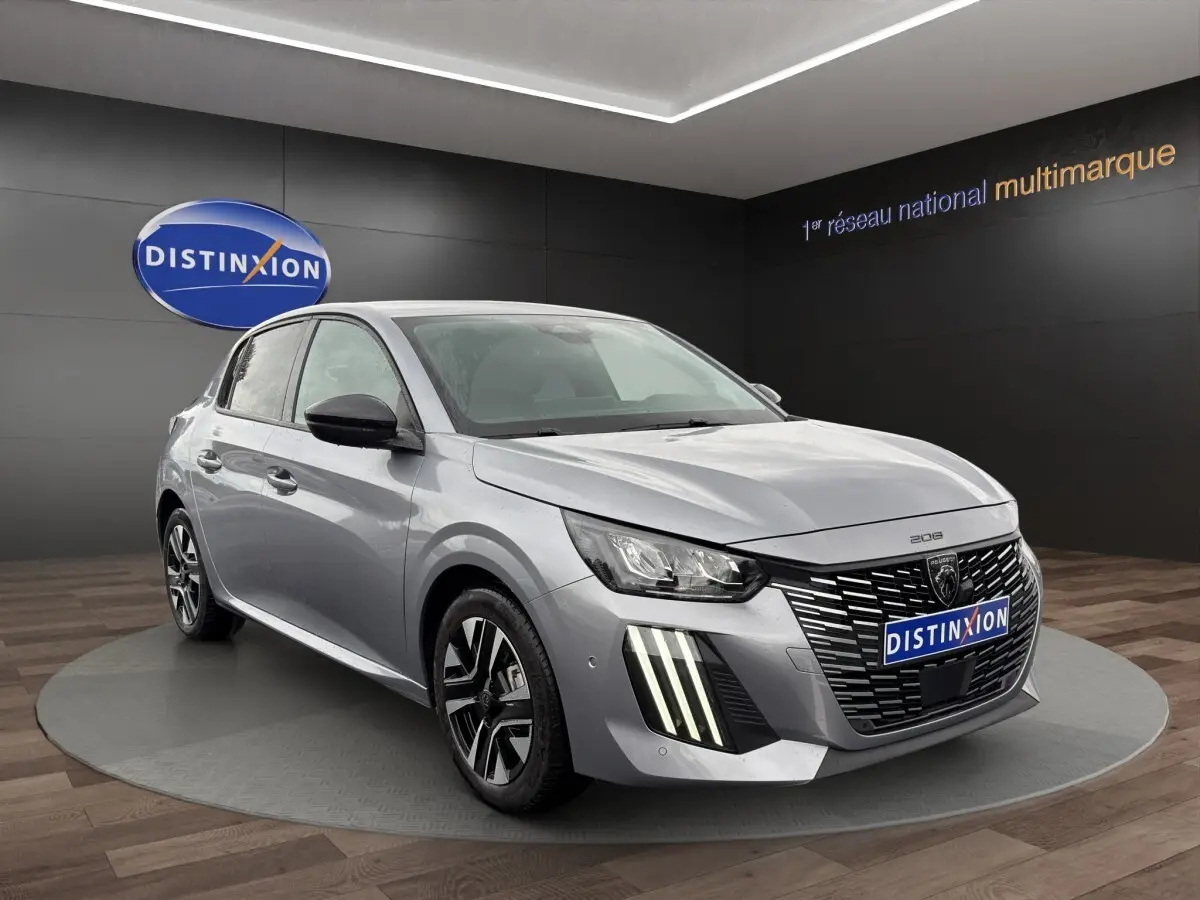 Peugeot 208 gris clair vue 3/4 avant droit, avec calandre distinctive et feux LED verticaux allumés.