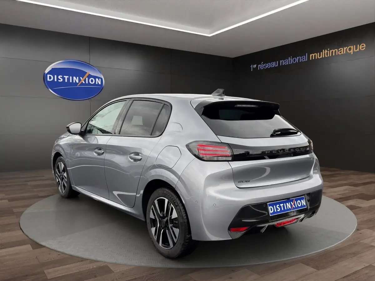 Peugeot 208 gris clair vue 3/4 arrière droit en intérieur, avec feux arrière LED et jantes alliage bicolores.
