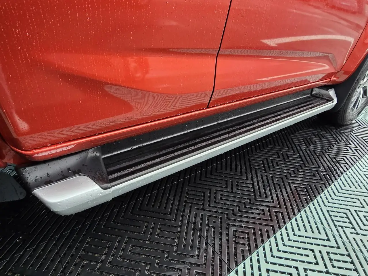 Vue latérale droite du pick-up Isuzu D-MAX orange métallisé, mettant en valeur le marchepied argenté et noir sous la porte.