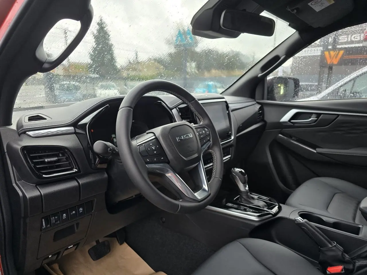 Intérieur de l'Isuzu D-MAX 2025 vu côté conducteur, volant cuir et console centrale avec levier de boîte auto.