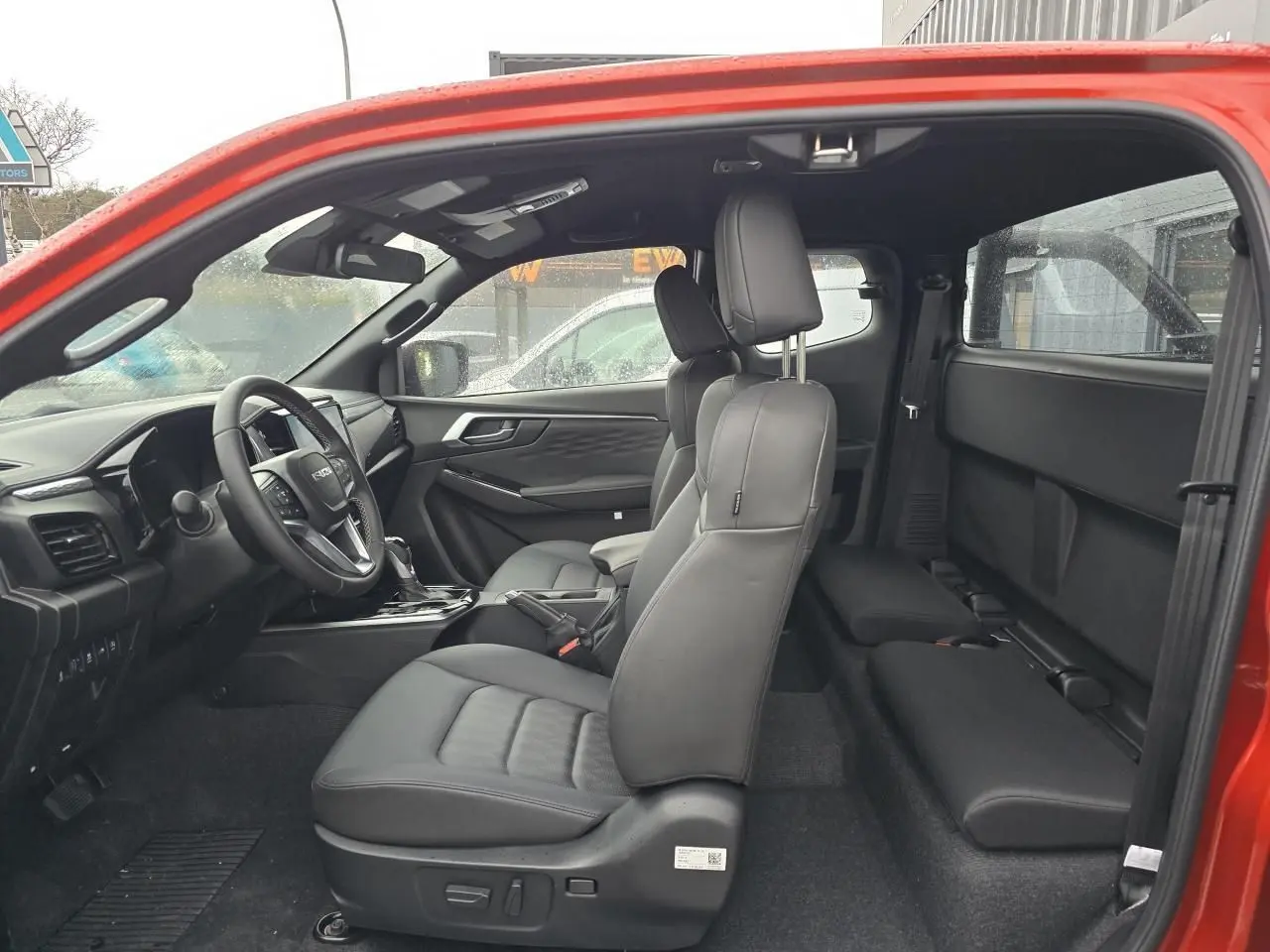 Vue intérieure côté gauche du pick-up Isuzu D-MAX orange métal, sièges en cuir noir et tableau de bord moderne.