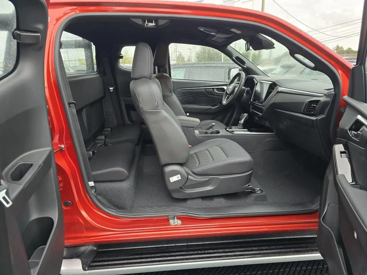 Intérieur côté droit du pick-up Isuzu D-MAX orange métal 2025, sièges en cuir noir et tableau de bord moderne.