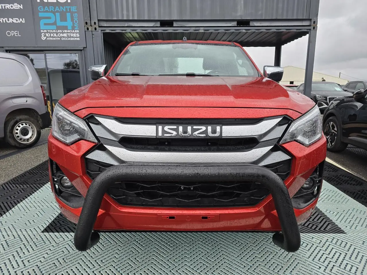 Vue frontale d'un Isuzu D-MAX orange métallisé avec bullbar noir et calandre chromée sous la pluie.