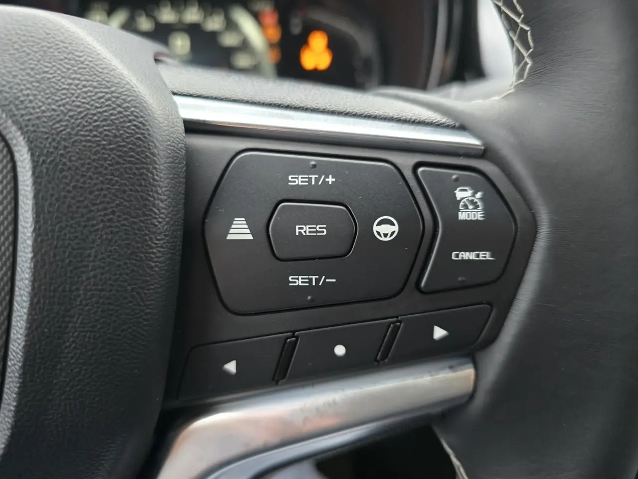 Gros plan sur les commandes au volant à droite de l'Isuzu D-MAX 2025, boutons noirs avec fonctions de régulateur et assistance.