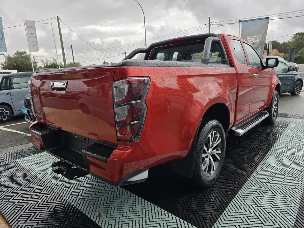 Vue 3/4 arrière droite d'un Isuzu D-MAX orange métallisé avec attelage et barres sport sur benne.