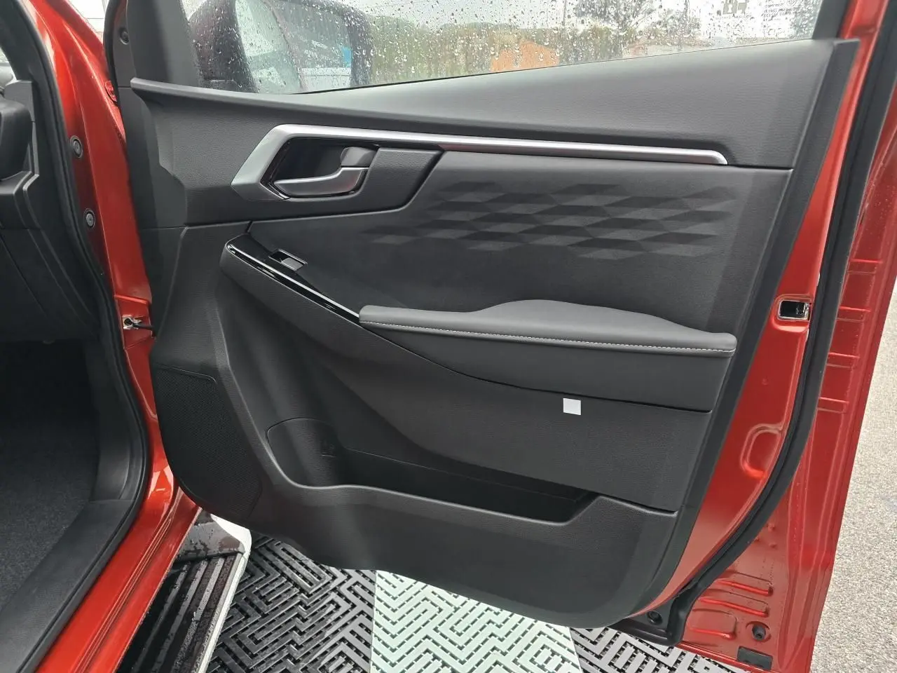 Porte côté gauche ouverte d'un Isuzu D-MAX orange métallisé, intérieur noir avec poignée et accoudoir design.