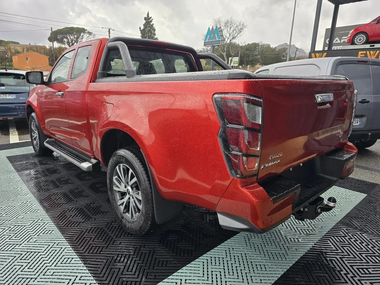 Vue 3/4 arrière droite d'un Isuzu D-MAX orange métallisé avec attelage et barre sport sur benne.