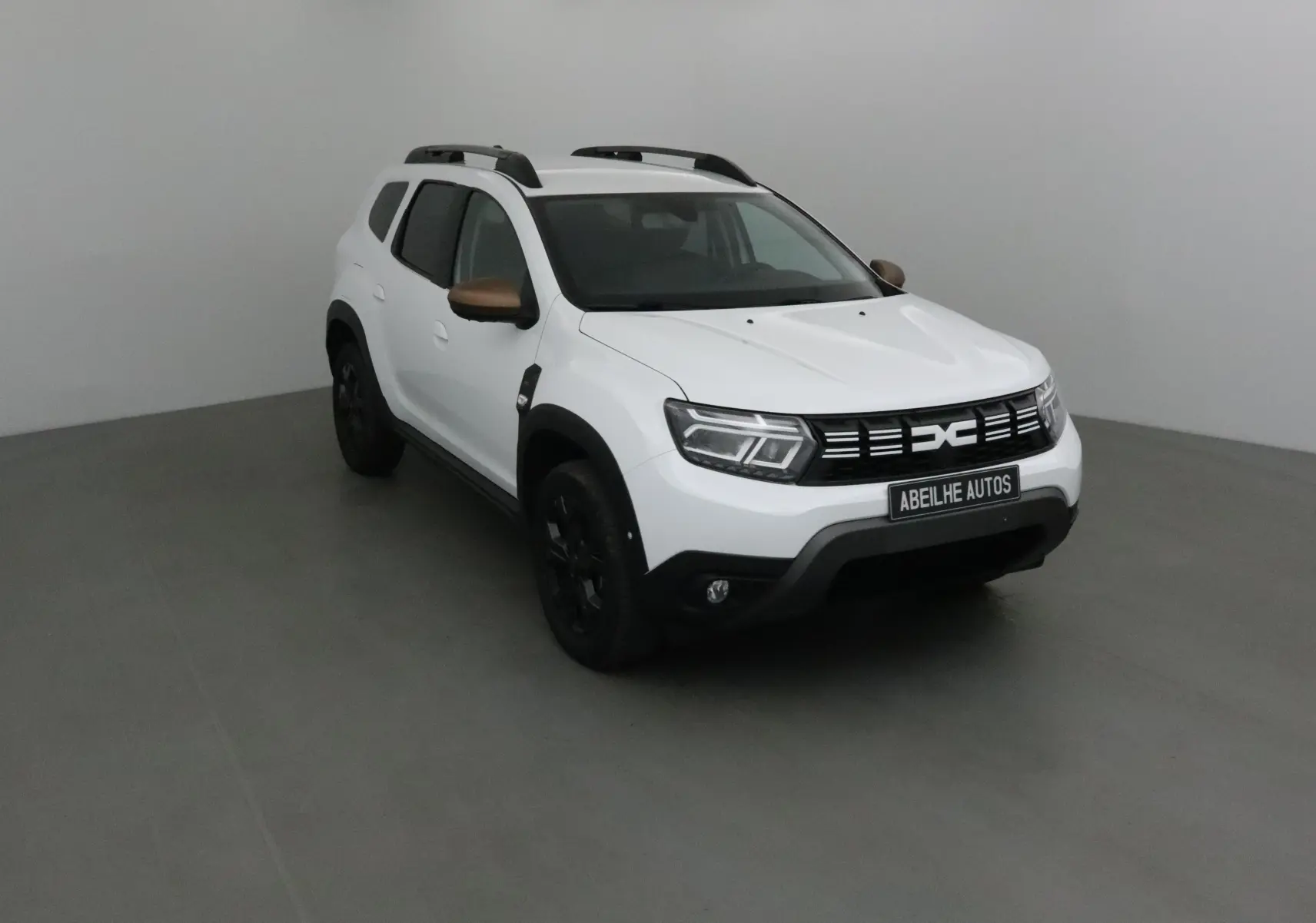 Dacia Duster blanc 4x4 vu en 3/4 avant droit avec rétroviseurs bronze et jantes noires.