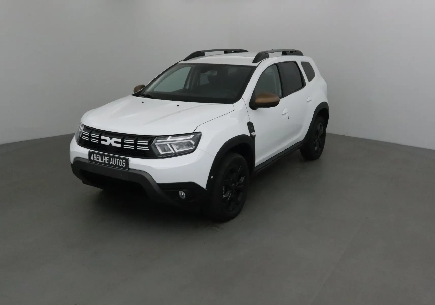 Dacia Duster 4x4 blanc en 3/4 avant droit avec coques de rétroviseurs bronze et jantes noires.