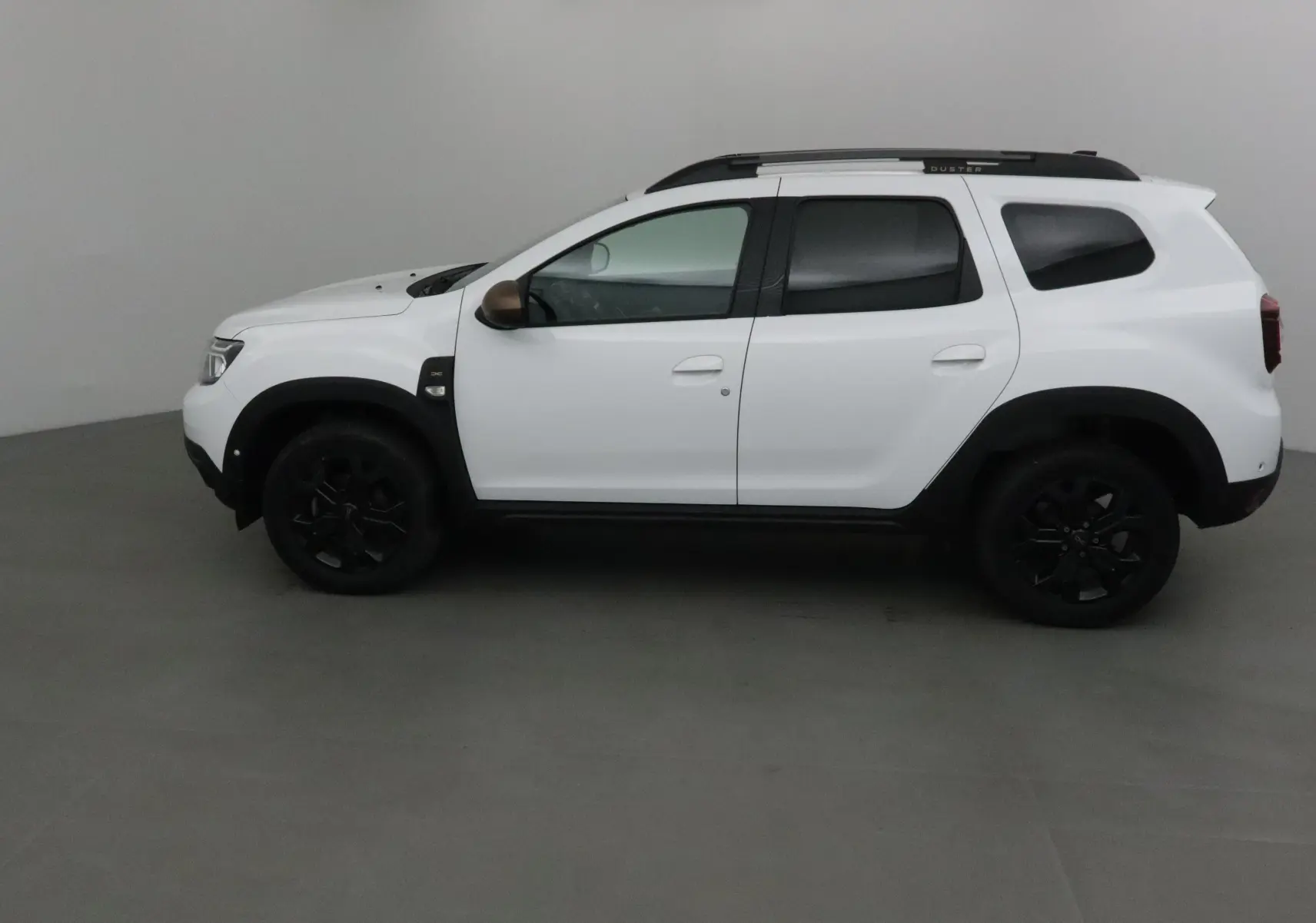 Profil côté gauche du Dacia Duster 4x4 blanc 2024 avec jantes noires et barres de toit noires marquées Duster.