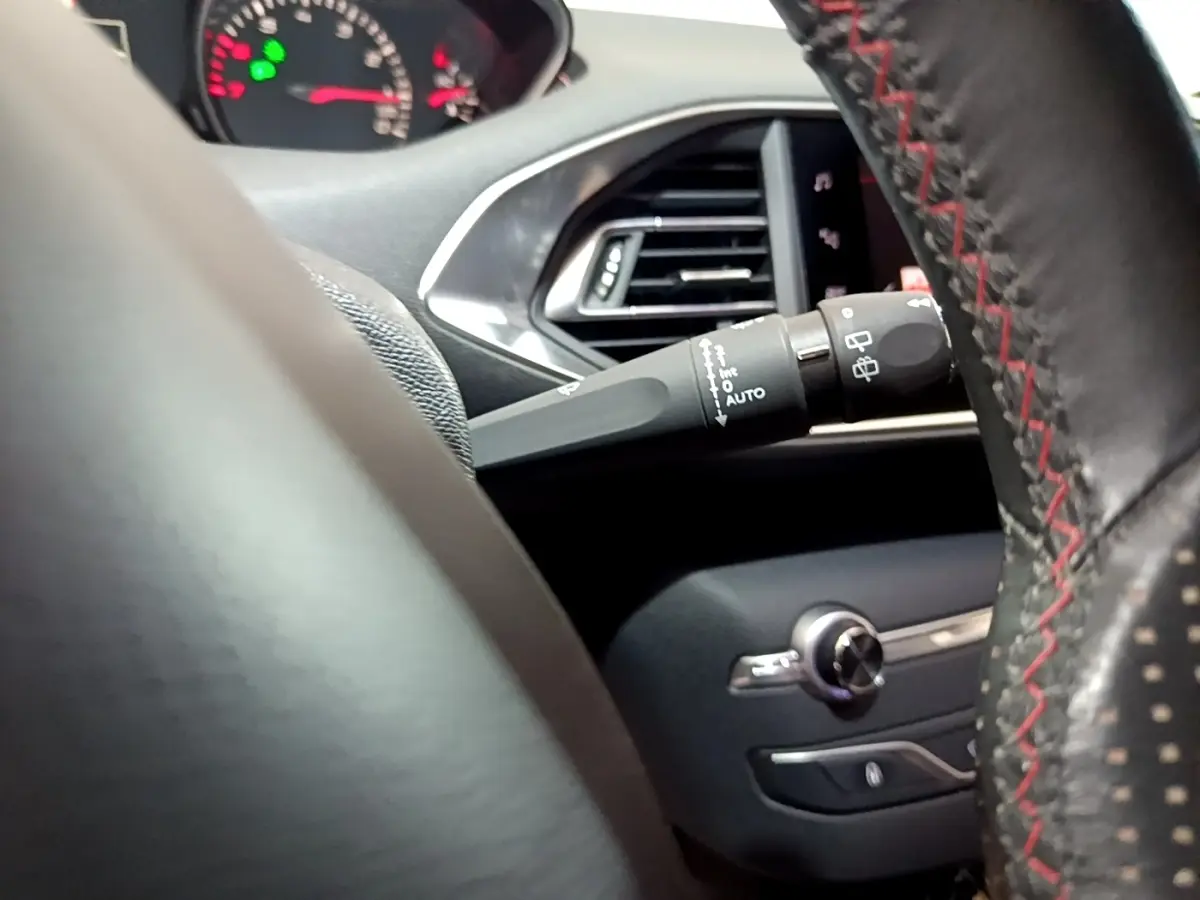 Détail intérieur du volant cuir noir avec surpiqûres rouges et commandes de la Peugeot 308 GT Line 2019.