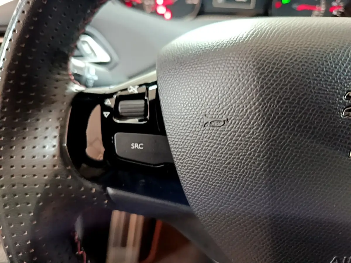 Gros plan sur le volant cuir perforé côté gauche du Peugeot 308 GT Line blanc avec commandes audio intégrées.