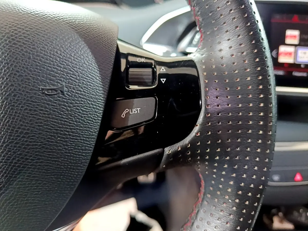 Gros plan sur le volant cuir perforé avec commandes intégrées du Peugeot 308 GT Line blanc, tableau de bord en arrière-plan.