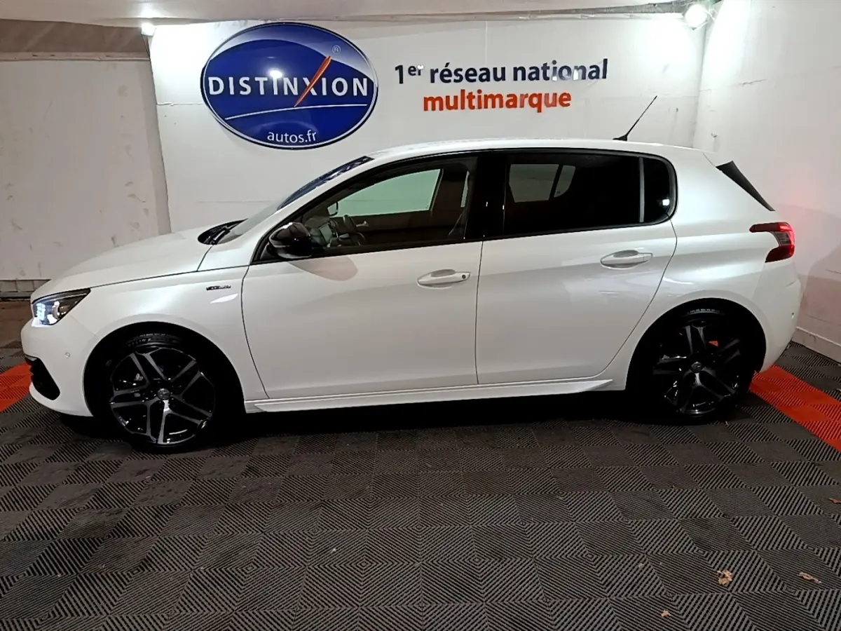 Profil côté gauche d'une Peugeot 308 Puretech 130 S&S GT Line blanche avec jantes noires dans un showroom.