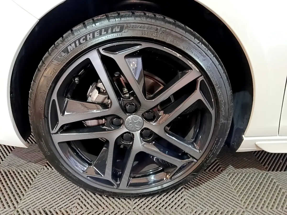 Gros plan sur la roue avant gauche noire brillante de la Peugeot 308 blanche Puretech 130 S&S GT Line 2019