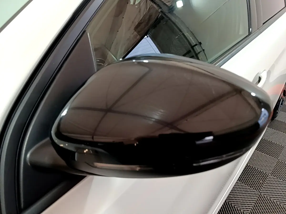 Gros plan sur le rétroviseur noir côté gauche d'une Peugeot 308 blanche, reflet du plafond visible.