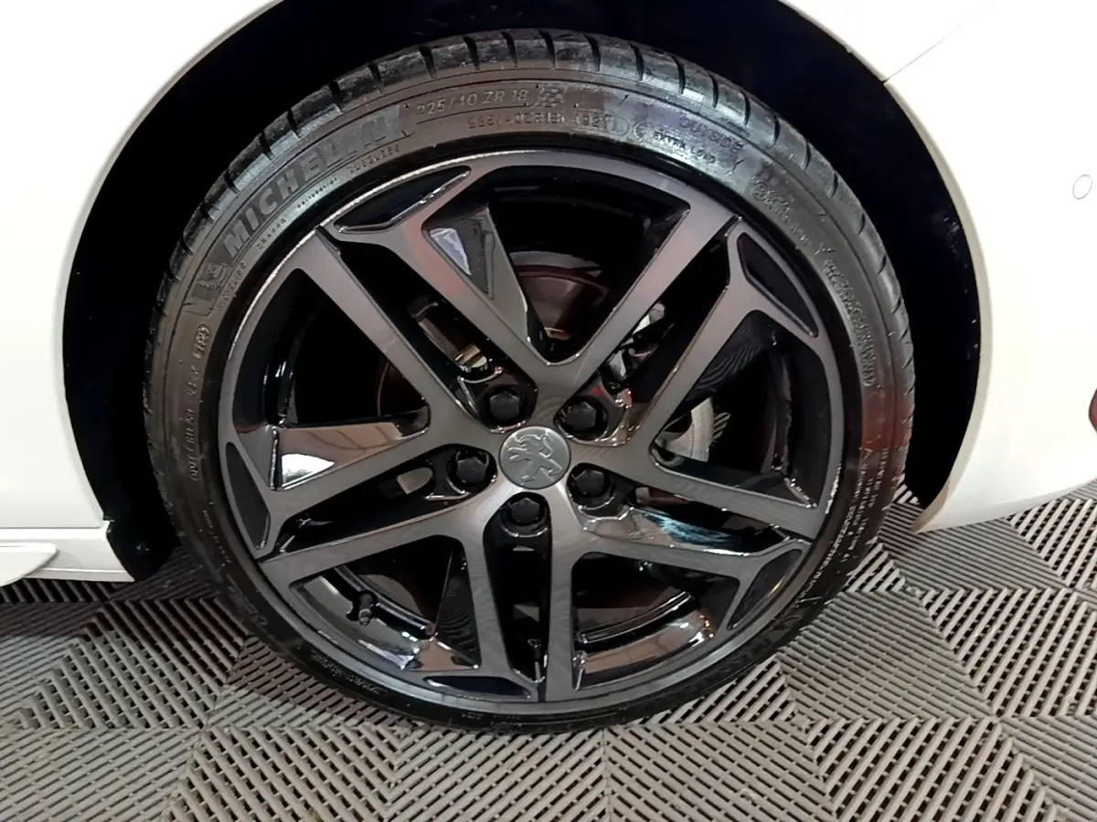 Gros plan sur la roue avant droite noire brillante d'une Peugeot 308 blanche Puretech 130 S&S GT Line 2019.
